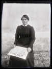 Portrait d'une femme en robe sombre assise, tenant le journal "Le petit journal" ouvert sur les genoux.