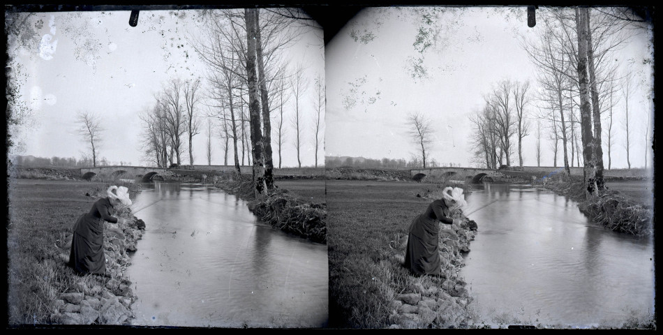 Femme pêchant au bord de l'Angillon à Vers-en-Montagne, le pont du Latet en arrière plan.