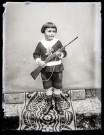 Portrait d'un petit garçon debout, une fausse carabine dans les mains.
