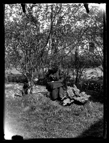 Femme assise jouant avec un chat noir dans un jardin.