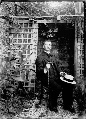 Un homme assis sur une chaise tenant sa canne et son chapeau