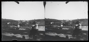 Maisons éparses et village dans un paysage vallonné.