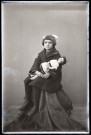 Portrait d'une fillette en manteau, assise une poupée dans les bras.