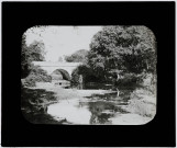 Reproduction d'une vue intitulée "Paysage près de Ploërmel", un militaire prend la pose près d'un petit pont.
