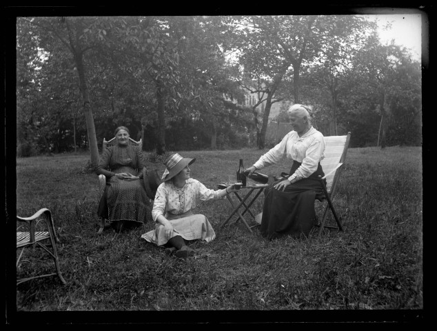Trois femmes assises dans un jardin se désaltèrent.