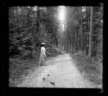 Femme vue de dos au bord d'un chemin forestier.